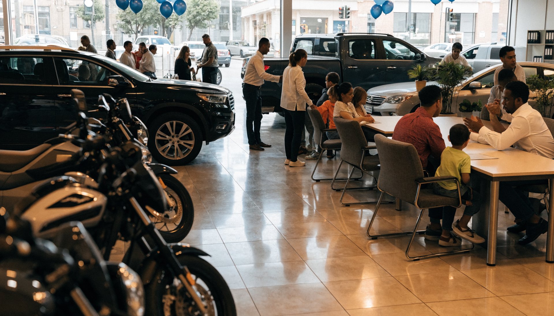 Showroom de revenda com carros, motos e clientes sendo atendidos por vendedores